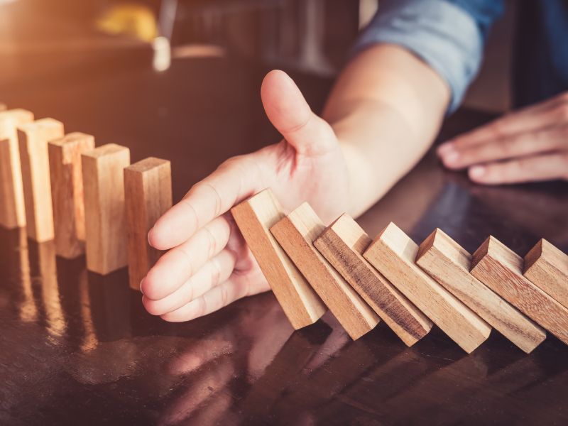 mano ferma dei blocchetti di legno che stanno cadendo a simbolo del prevenire i rischi aziendali