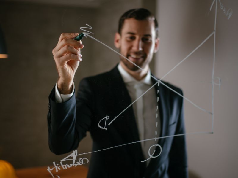 uomo segna con il pennarello un grafico finanziario su una lavagna trasparente