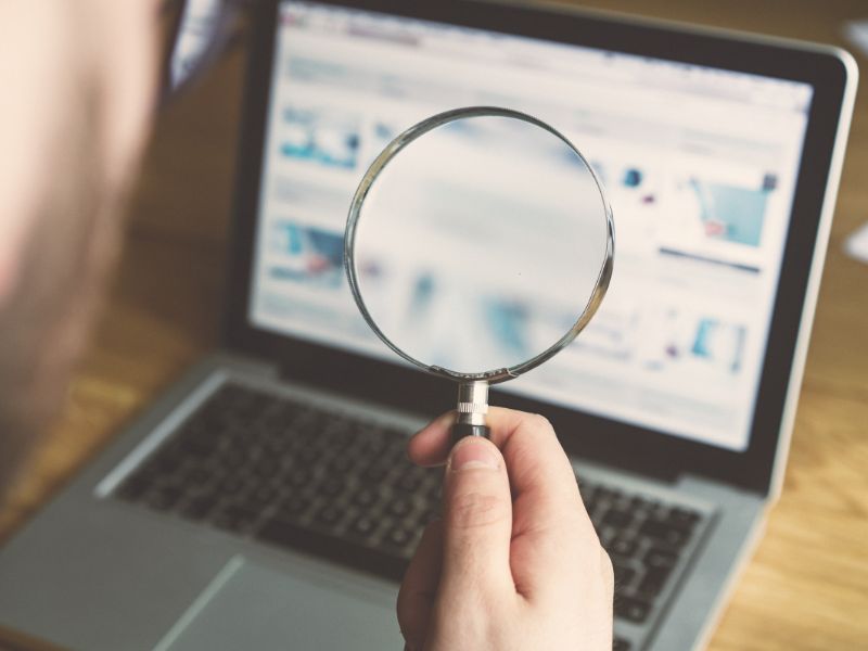 uomo con lente di ingrandimento guarda al computer dei grafici finanziari